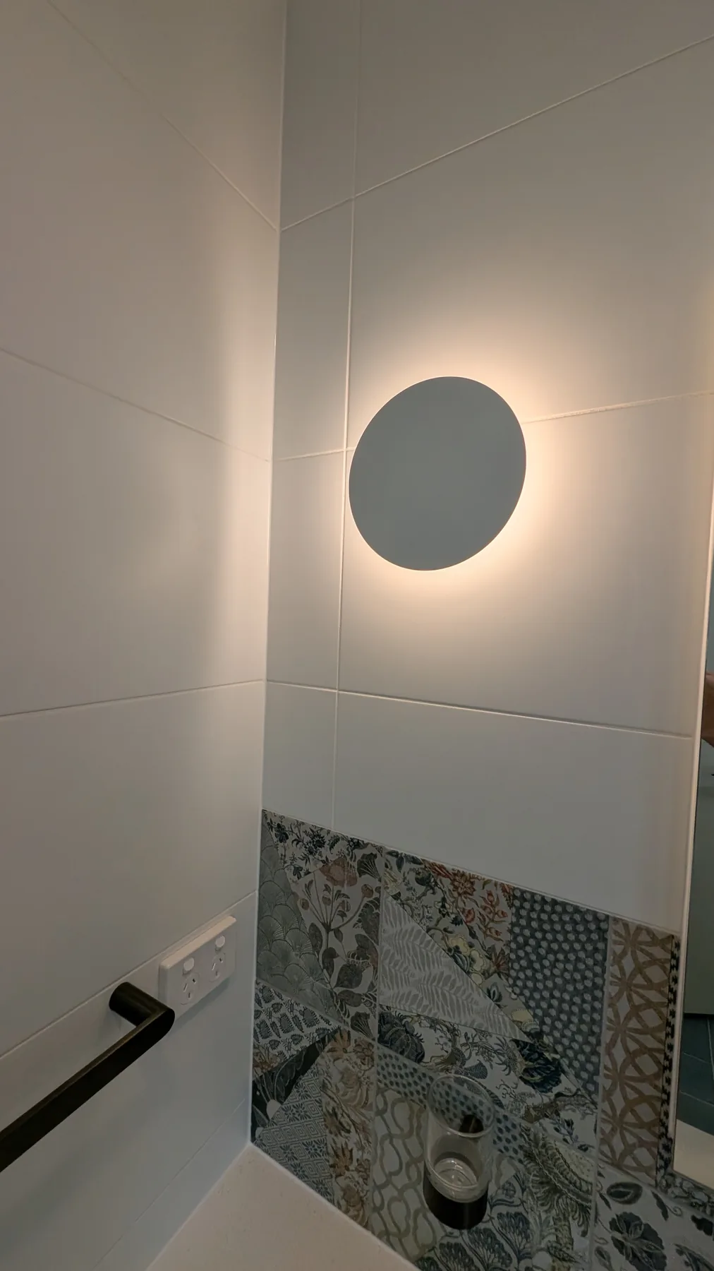 Backlit circular wall sconce over patterned bathroom tile